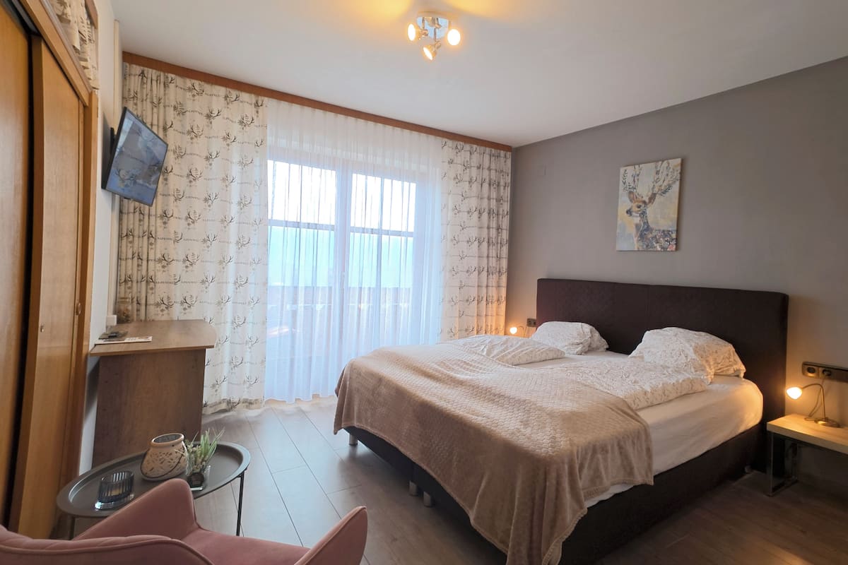 Une chambre à coucher avec un lit, des tables de chevet, un bureau, une chaise et une fenêtre avec des rideaux.