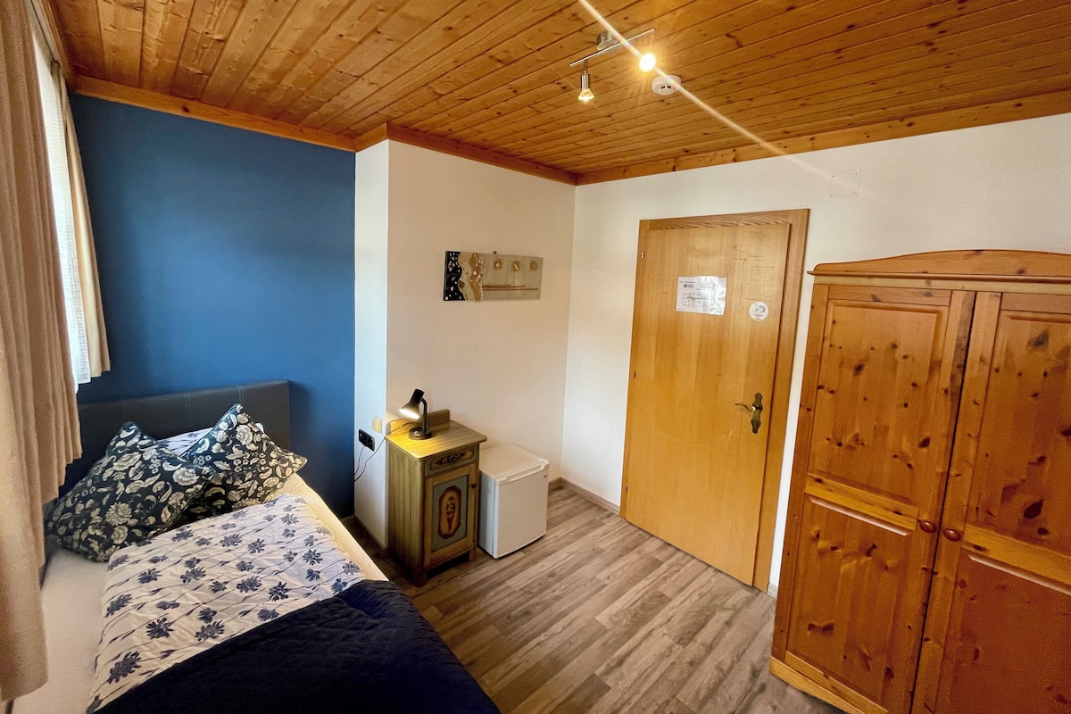 Une chambre à coucher comprenant un lit, une commode, un petit réfrigérateur et une armoire en bois.