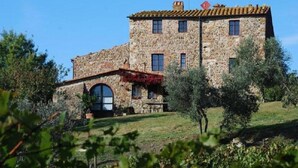 A stone building with a tiled roof, arched windows, and a small balcony with red vines. - Agriturismo La Colombaia (Massa Marittima)