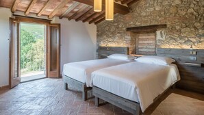A bedroom with two beds, stone walls, wooden beams, and a balcony with a view. - Agriturismo La Colombaia (Massa Marittima)