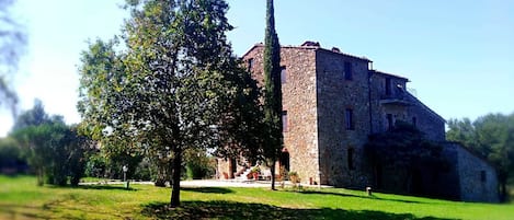 A stone building with a central tower, surrounded by a grassy area and trees.