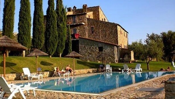 A pool area with lounge chairs and umbrellas, surrounded by a stone building and tall trees. - Agriturismo La Colombaia (Massa Marittima)