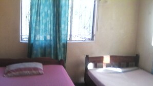 Une chambre avec deux lits, dont un plus grand et un plus petit, ainsi qu’une fenêtre et des rideaux.