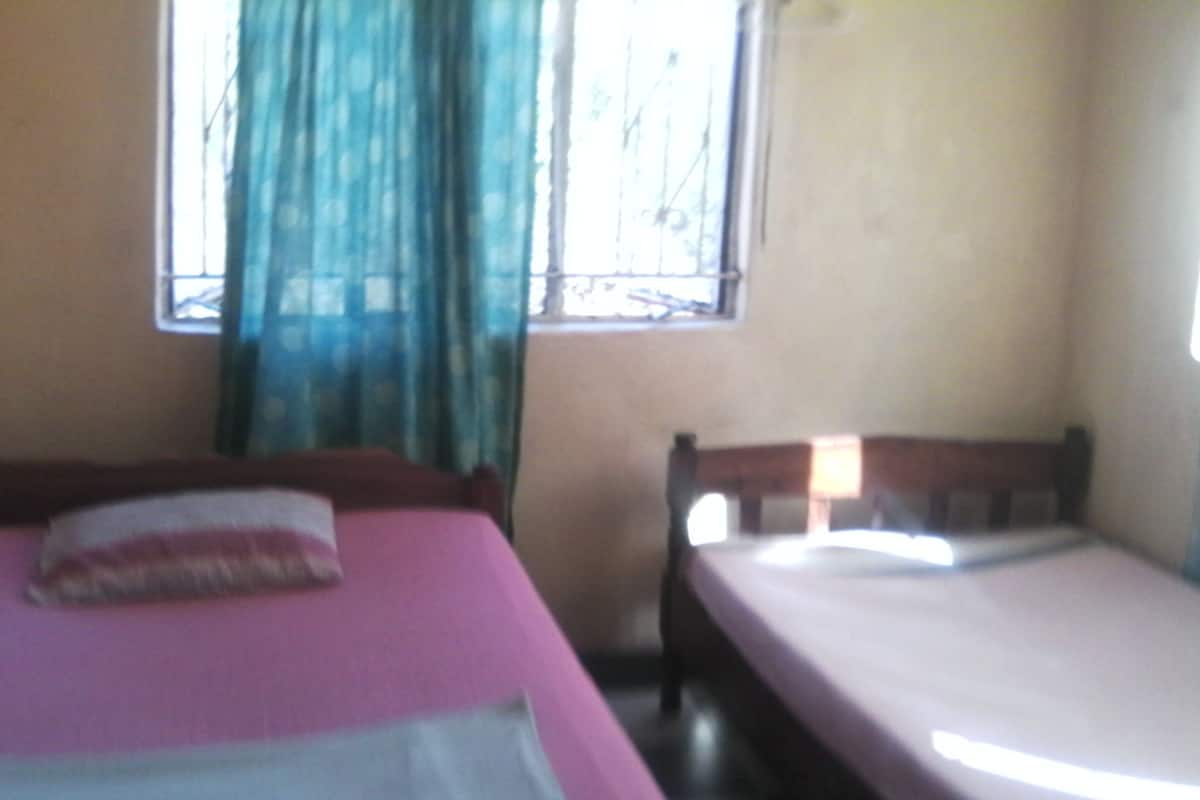A room with two beds, one larger and one smaller, with a window and curtains.