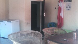 Une pièce comprenant une table à manger, des chaises en osier, un réfrigérateur et une porte donnant sur une autre pièce.