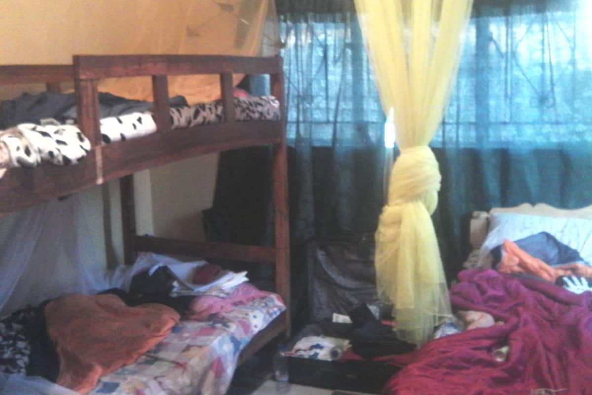 A bunk bed with a wooden frame, a lower bed with a colorful blanket, and a canopy with yellow fabric.