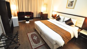 A hotel room with a bed, a desk, a chair, a sofa, and a TV. - Phoenicia Hotel (Dubai)