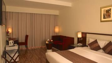 A hotel room with a bed, a desk with a chair, a sofa, a lamp, and a painting on the wall.