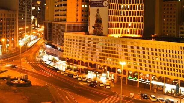 A modern building with a large circular structure on top, featuring illuminated signage and a statue. - Phoenicia Hotel (Dubai)