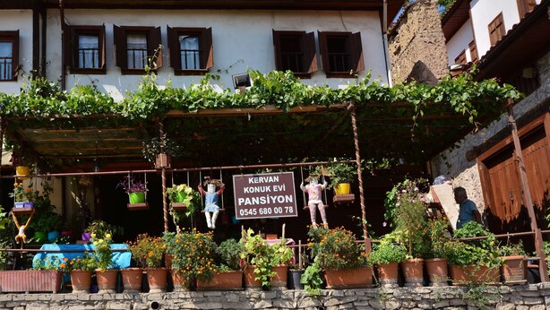 Un edificio con letrero, plantas en macetas y un muro de piedra.