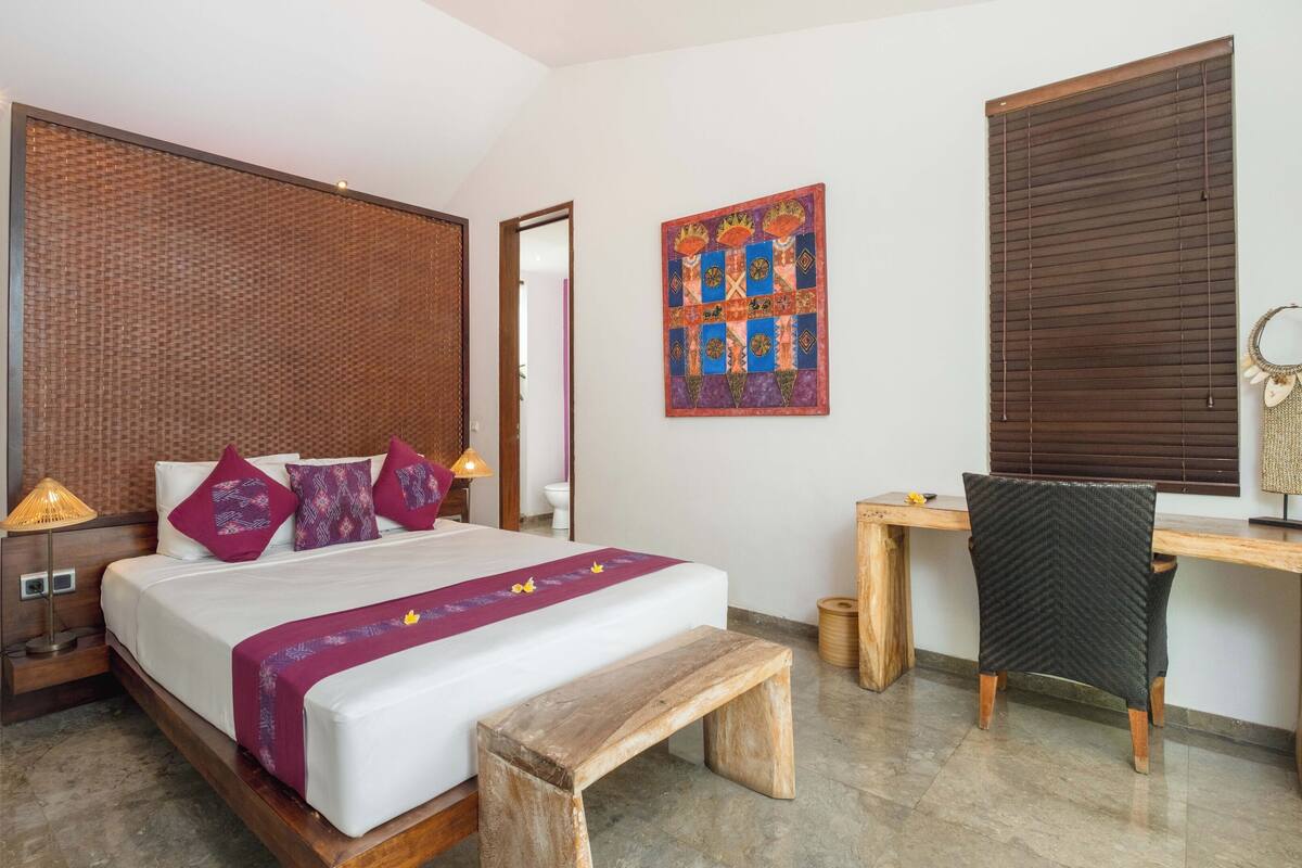 Un dormitorio con cama, mesitas de noche, escritorio, silla y un adorno en la pared.