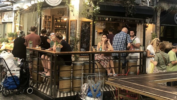 A rustic outdoor café with a checkered floor, wooden barrels, and hanging plants. - Peaceful  Windows of Jerusalem (Jerusalem)