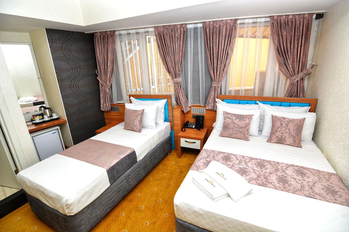 A hotel room with two single beds, a small desk with a chair, a telephone, and a window with curtains.