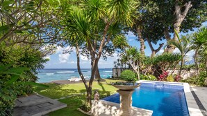Zona de piscina con vistas al océano, rodeada de plantas y árboles tropicales.