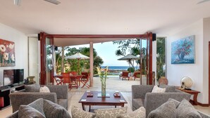 Amplia sala de estar con un gran sofá, una mesa de centro y un televisor. Cuenta con una zona de patio con muebles de exterior y vistas al océano.