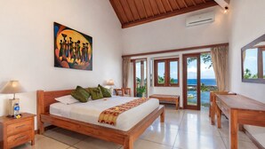 Un dormitorio amplio con una cama grande, muebles de madera, un cuadro en la pared y vistas al océano.