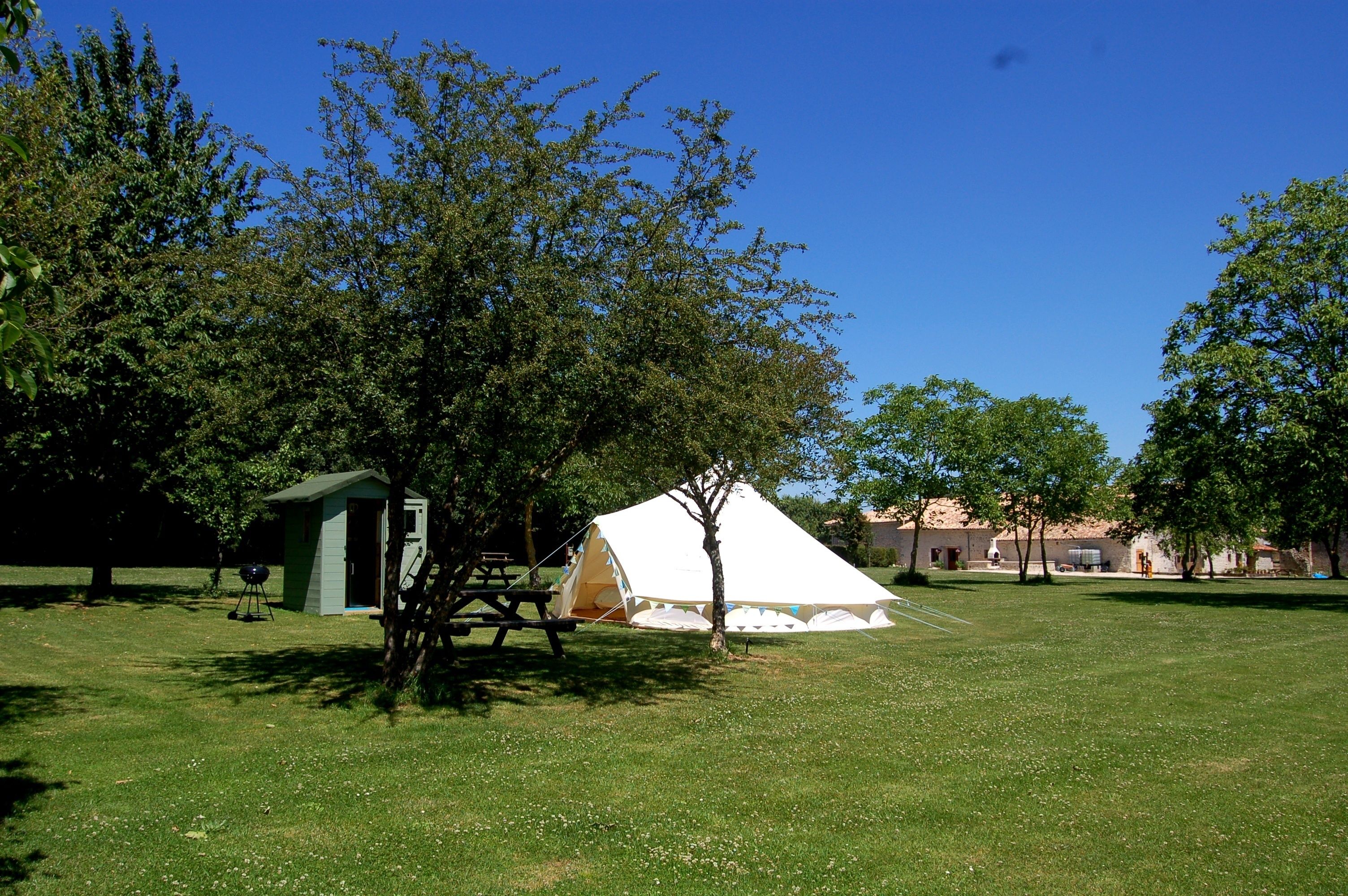 A grassy field with a white tent, a small shed, and a picnic table.