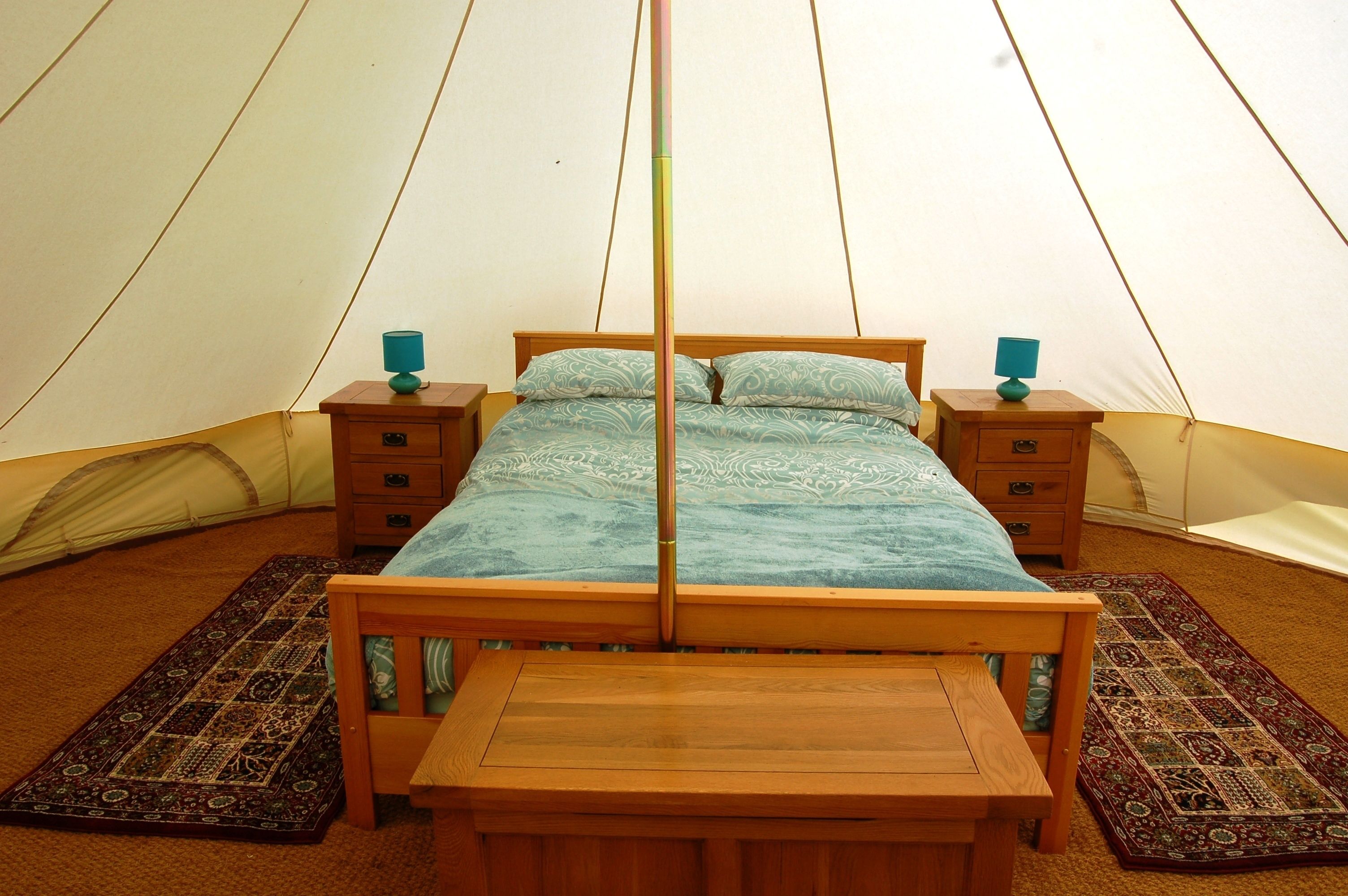 A tent with a bed, two bedside tables, and a wooden bench.