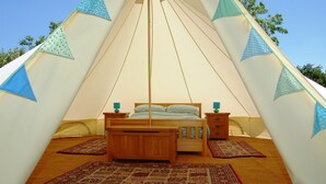 Una tienda de campaña con cama, mesitas de noche de madera y alfombras estampadas.
