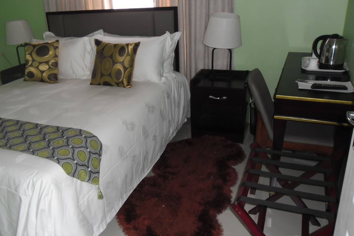 A hotel room with a bed, bedside table, lamp, and a red furry rug.