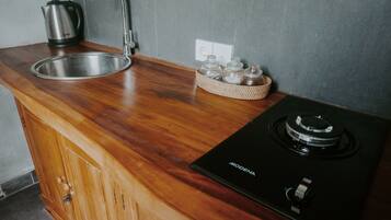 A kitchen with a stainless steel sink, a kettle, a stove, and a woven basket with jars.