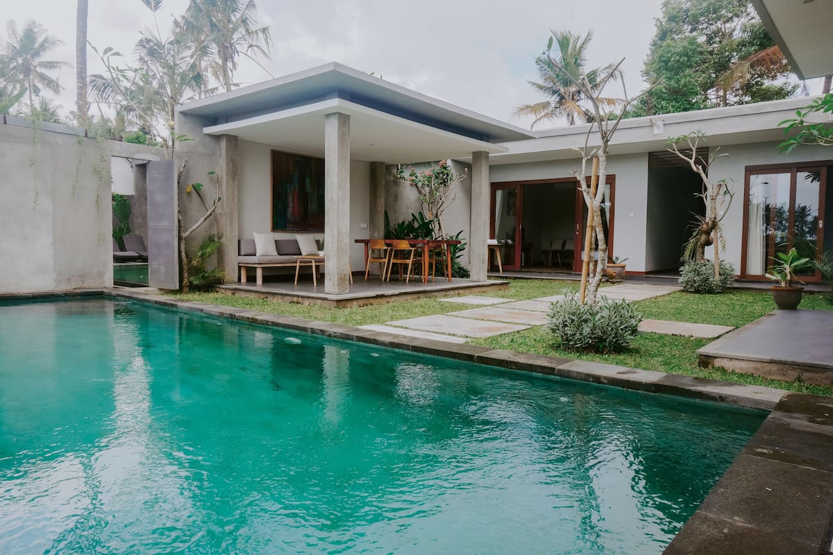 A modern house with a swimming pool, outdoor seating, and lush greenery.