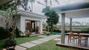 Een modern huis met een patio, een zwembad en weelderige begroeiing.