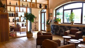 A cozy interior with wooden floors, a variety of wine bottles on shelves, comfortable seating, and large windows offering natural light. - Guest House Terra di Venera (Acireale)