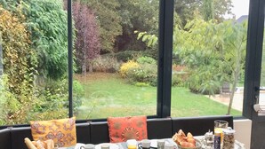 A breakfast table set with various food items and drinks, overlooking a garden with trees and a lawn. - Maison d’hôtes Joussaume Latour (Chateau-Thierry)
