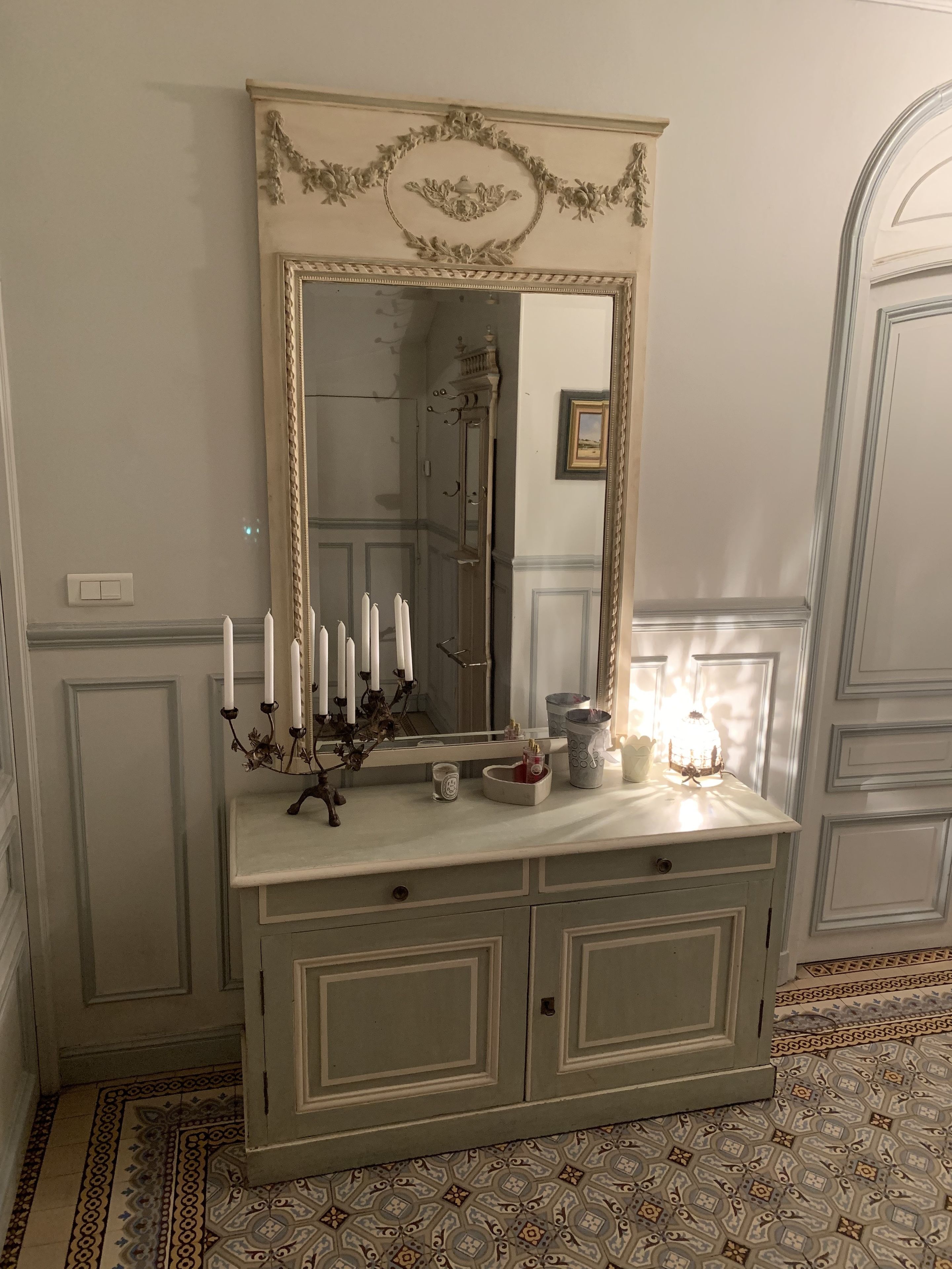Een vintage kaptafel met een grote spiegel, kaarshouders en decoratieve objecten.