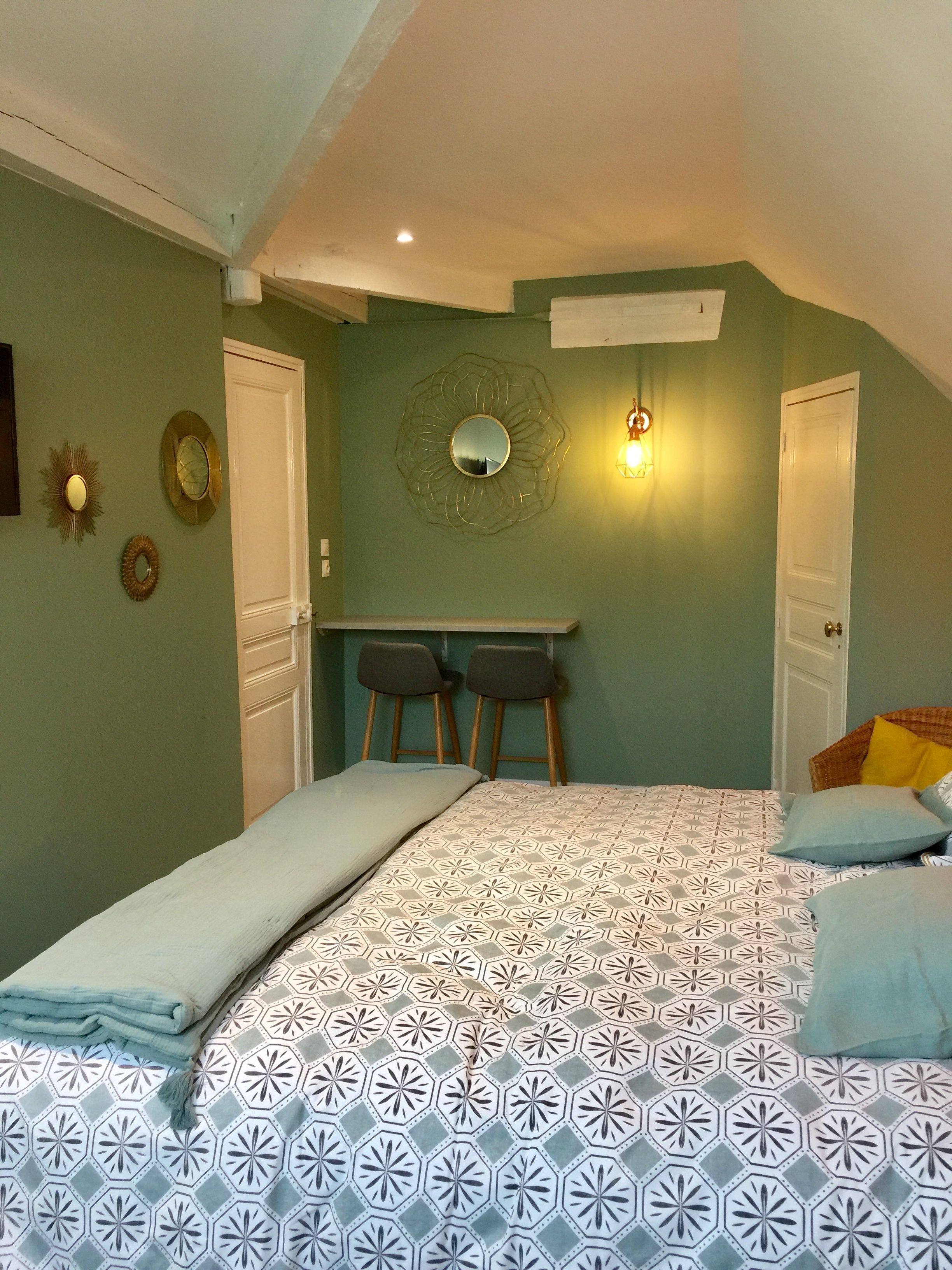 Een slaapkamer met een bed, een bureau, twee stoelen, een spiegel en een wandlamp.