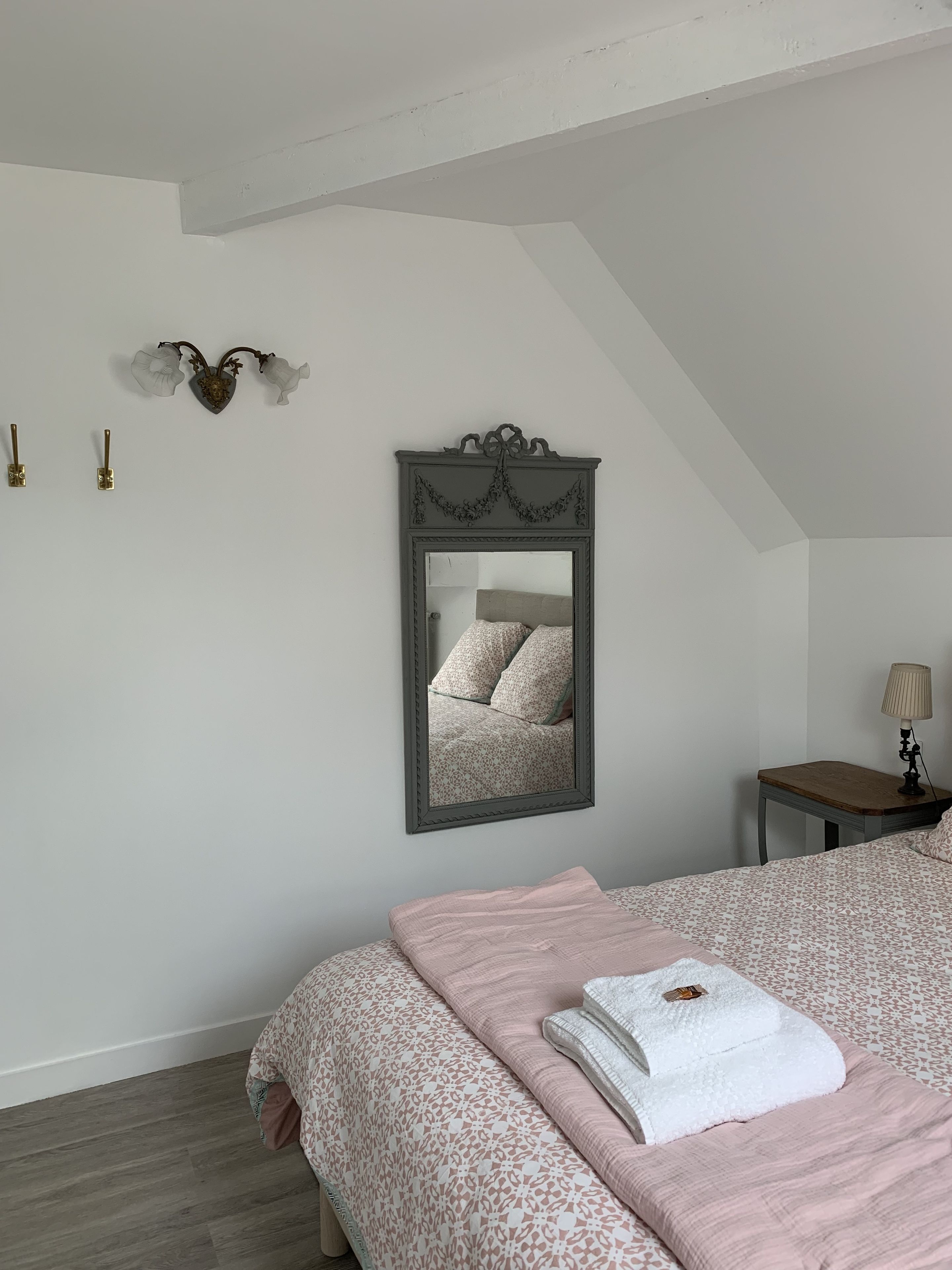 A bedroom with a bed, a nightstand, a lamp, and a mirror on the wall.