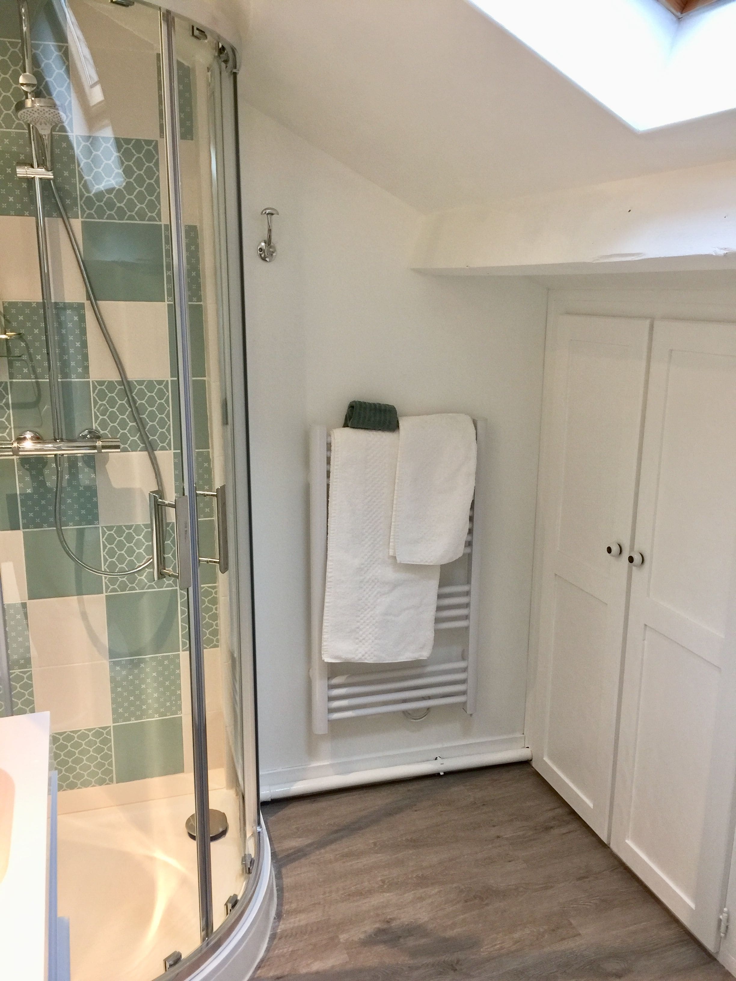 Een douche met een glazen deur, een handdoekhouder met twee handdoeken en een witte deur met twee handgrepen.