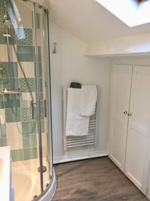 Ducha con mampara de vidrio, barra de toallas con dos toallas y puerta blanca con dos pomos.