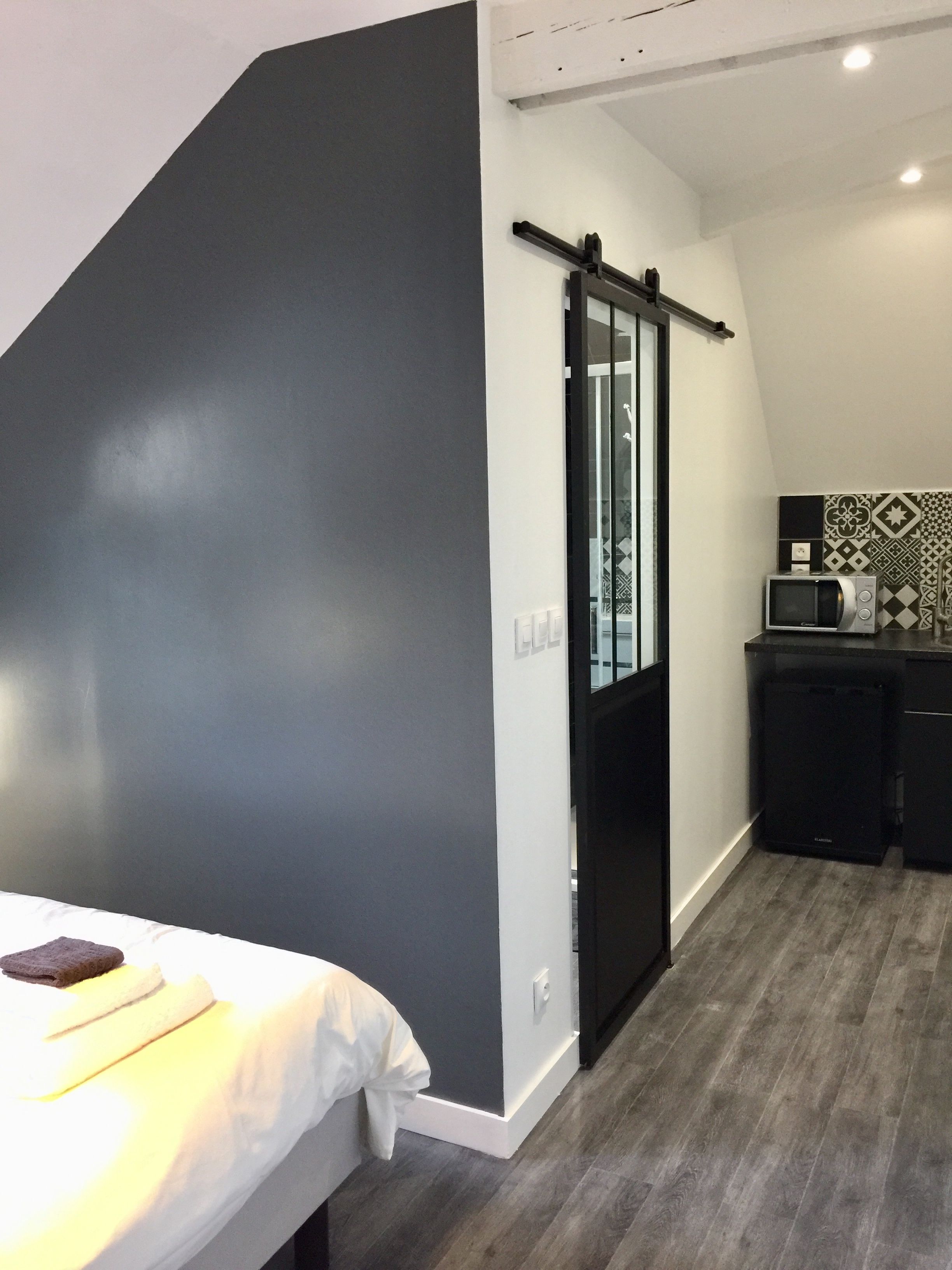Une pièce de taille modeste comprenant un lit, une petite kitchenette, une porte coulissante et un mur décoré d’un motif.