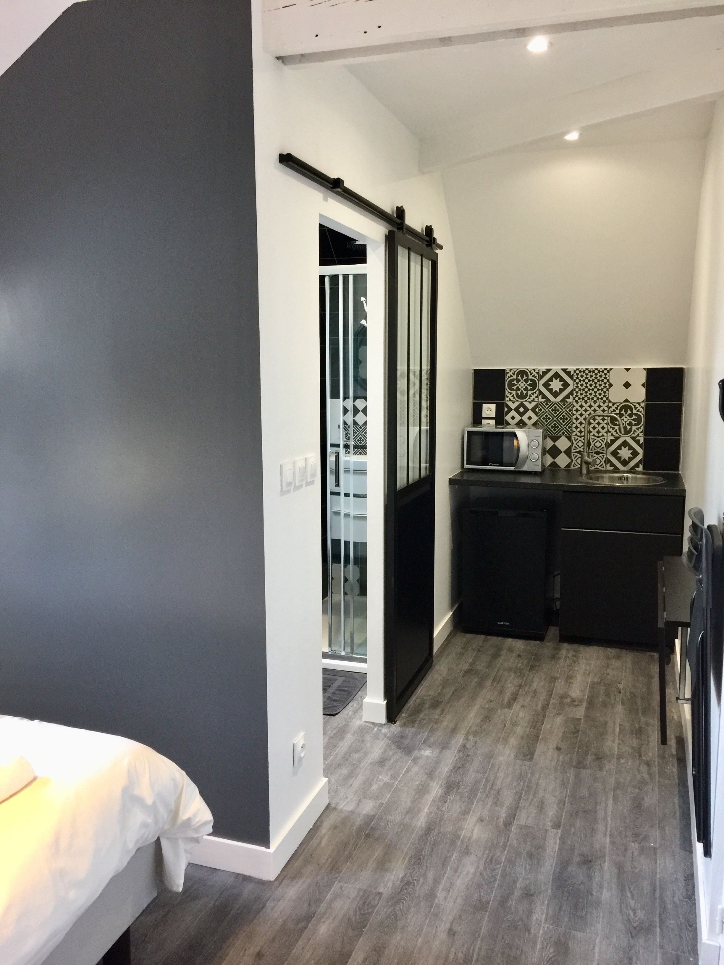 Una habitación de hotel compacta con cama, kitchenette y puerta corredera a un balcón.