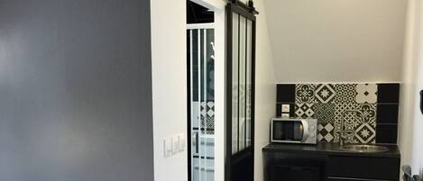 Una habitación de hotel compacta con cama, kitchenette y puerta corredera a un balcón.