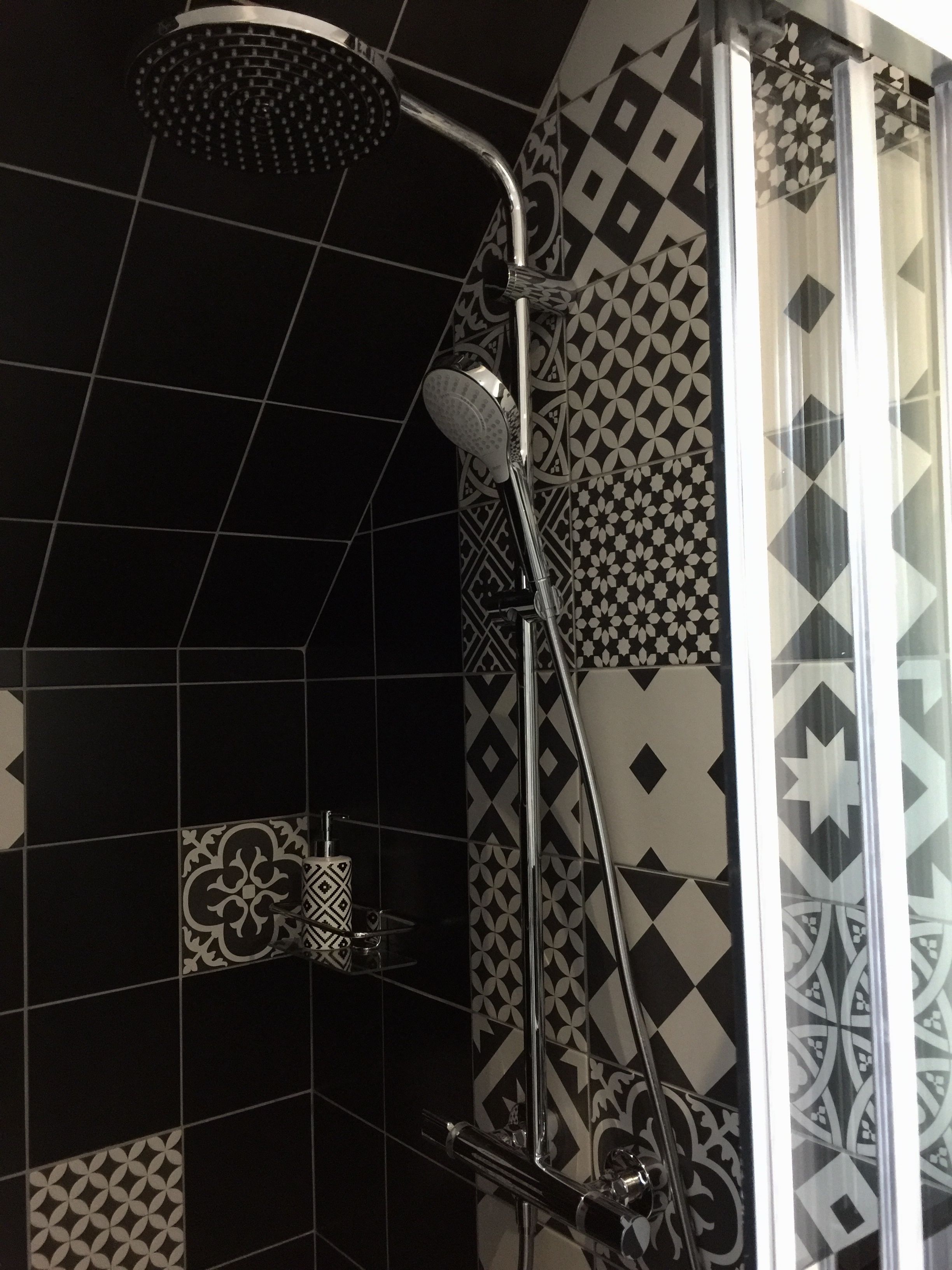 Una ducha con cabezal de ducha manual y cabezal de ducha lluvia, un box de ducha con paredes de vidrio y baldosas en blanco y negro con diseño en las paredes.