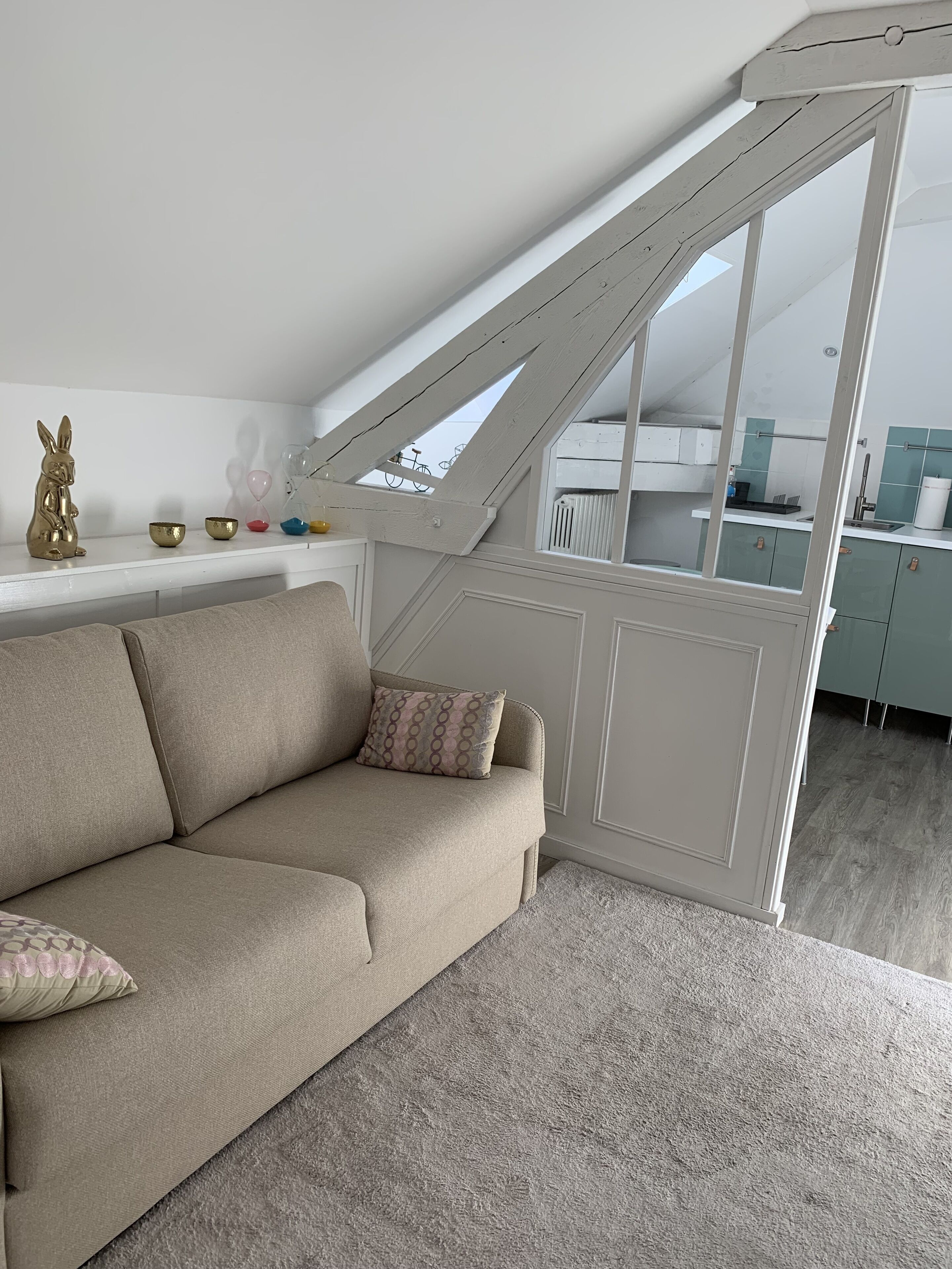 Un espai tipus loft amb sostre alt, cuina integrada i sofà beix amb coixins estampats.