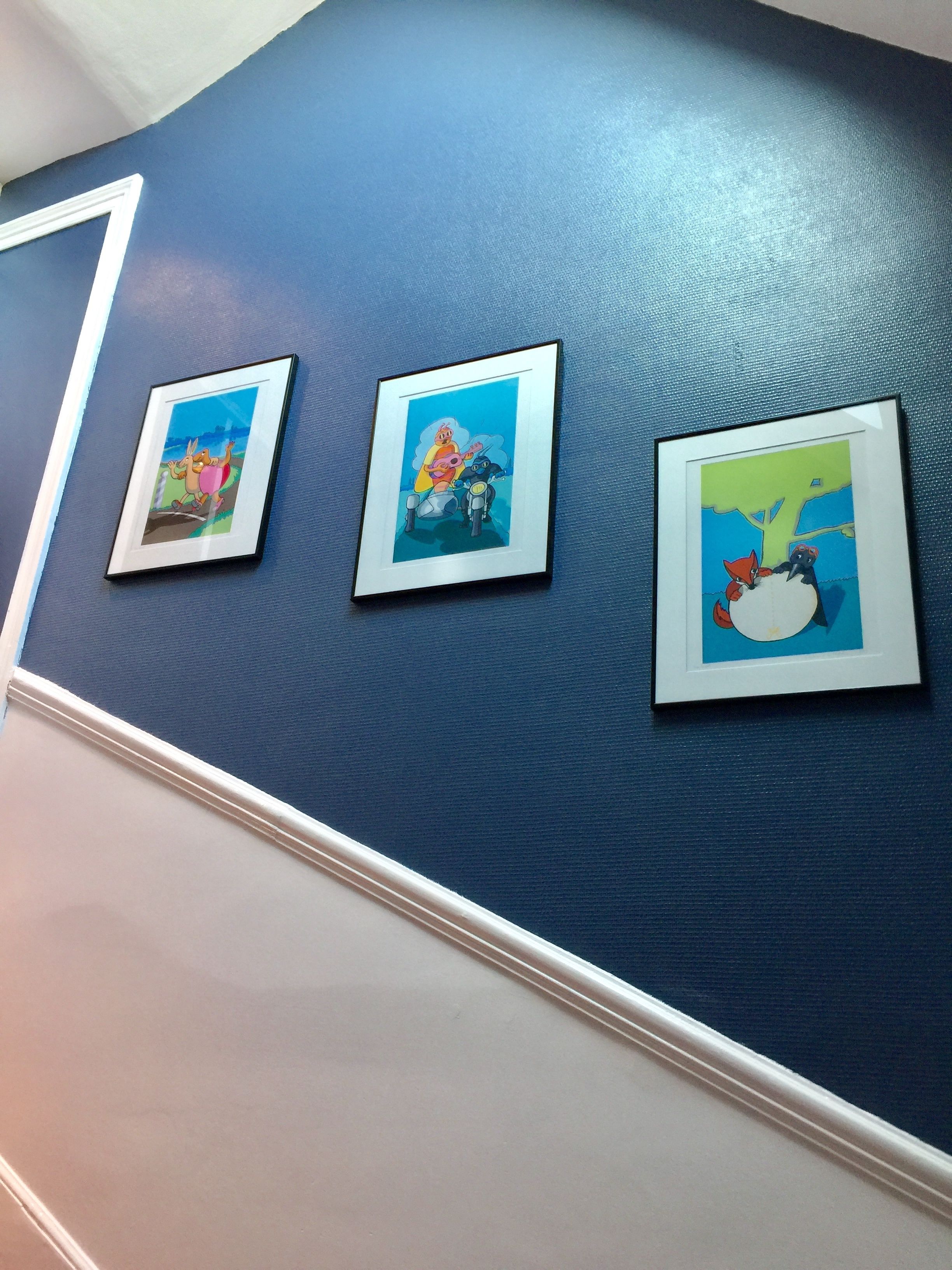 Three framed artworks on a blue wall.