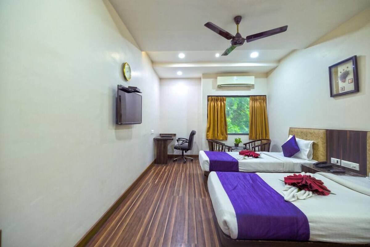 Quarto de hotel com duas camas, uma escrivaninha, uma cadeira, televisão e ventoinha no teto.
