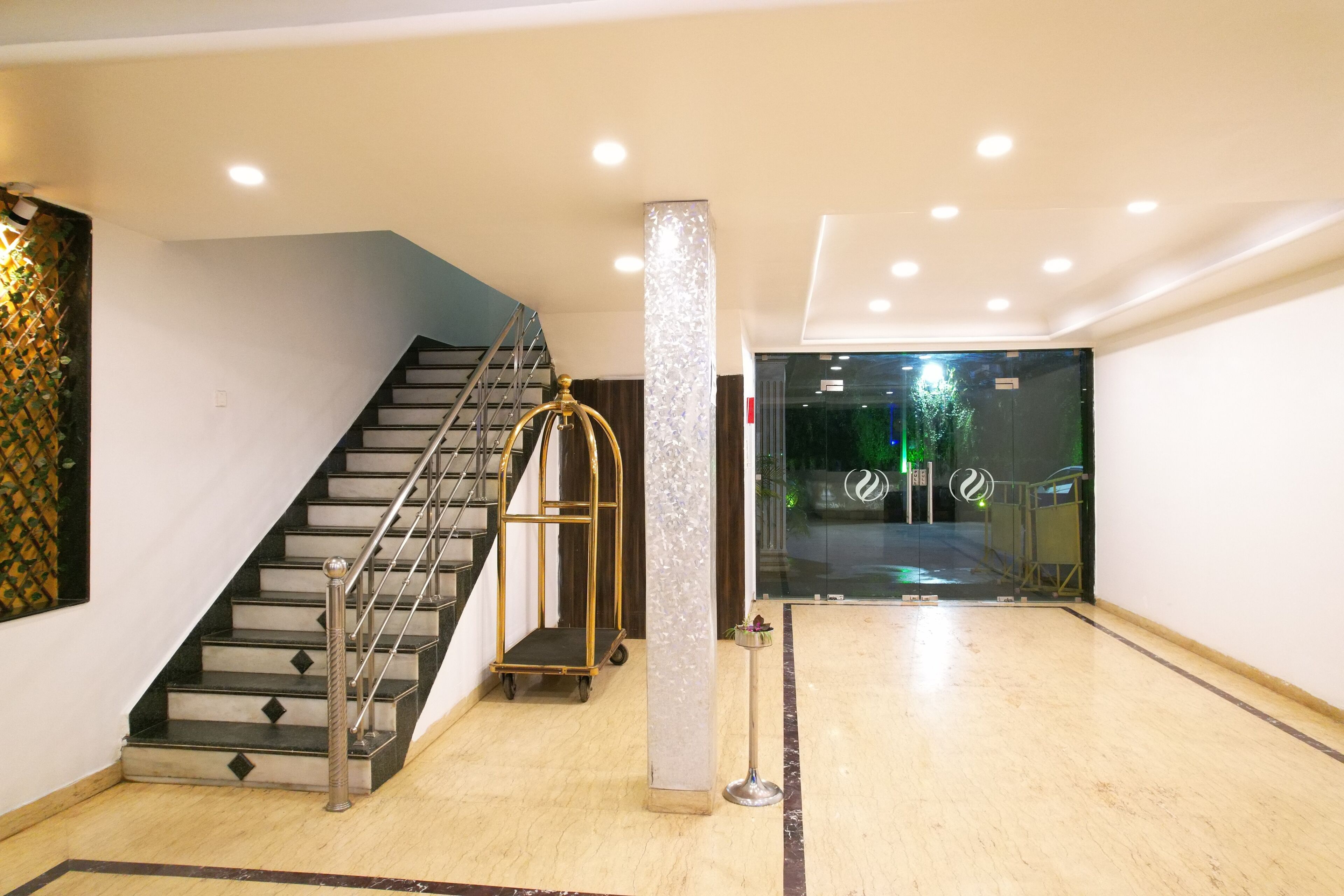 A hotel lobby with a marble floor, a staircase with metal railings, and a glass door leading outside.