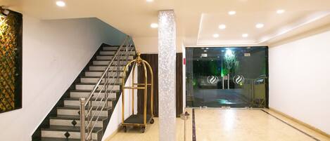 A hotel lobby with a marble floor, a staircase with metal railings, and a glass door leading outside.