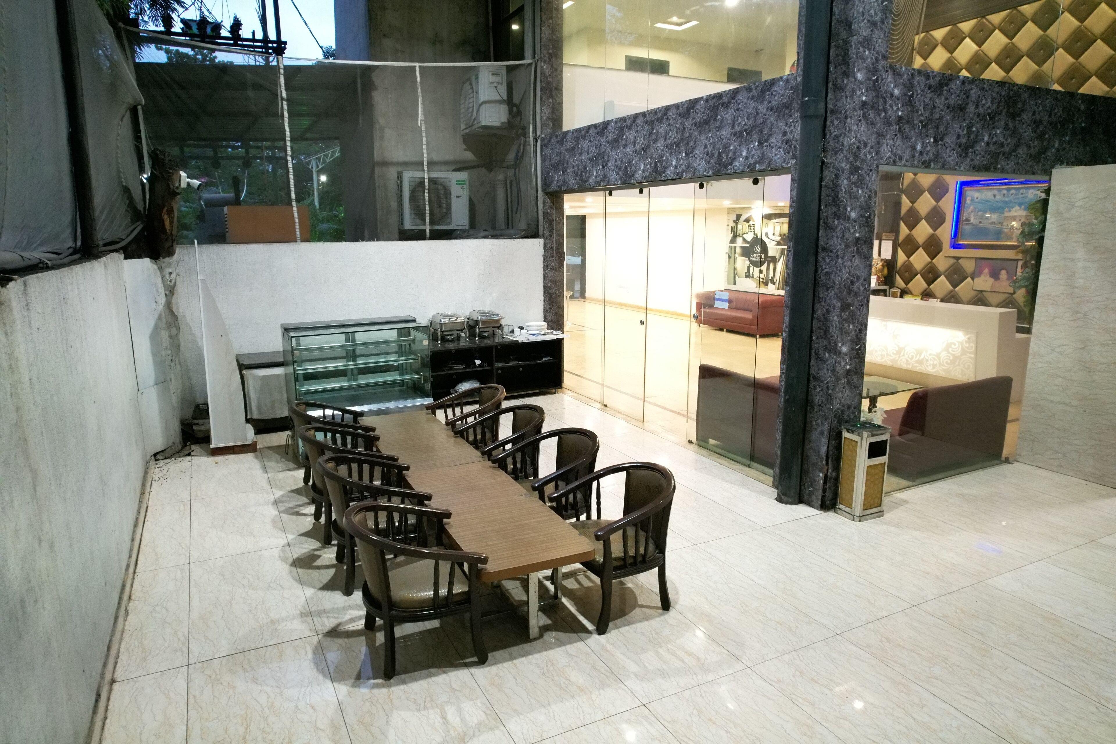 A dining area with a long wooden table and chairs, a glass partition, and a seating area with a sofa and a small table.