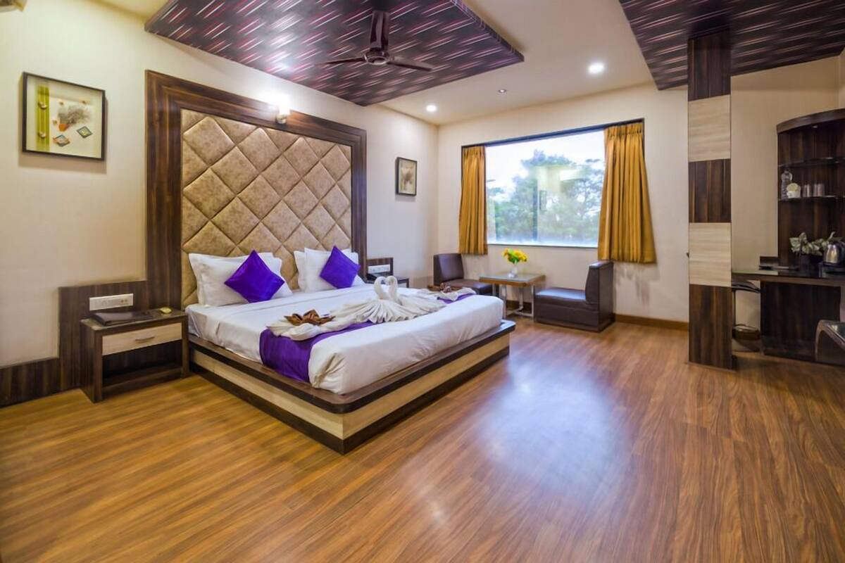 Quarto de hotel com cama grande, escrivaninha, cadeira e vista para o exterior.