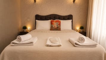 Una cama bien hecha con un cojín decorativo, dos lámparas de noche y una planta pequeña en una mesita.