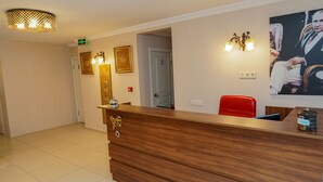 A hotel reception area with a wooden reception desk, a red chair, and a painting on the wall. - Pelit Boutique Hotel (Adalar)