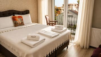 A hotel room with a large bed, a view of the city through the window, and a balcony with a chair.