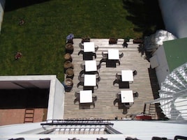 Un patio al aire libre con mesas y sillas, una terraza de madera y plantas en macetas.