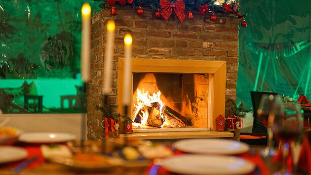 A fireplace with a fire, surrounded by Christmas decorations and a dining table set with plates and candles. - Pelit Boutique Hotel (Adalar)